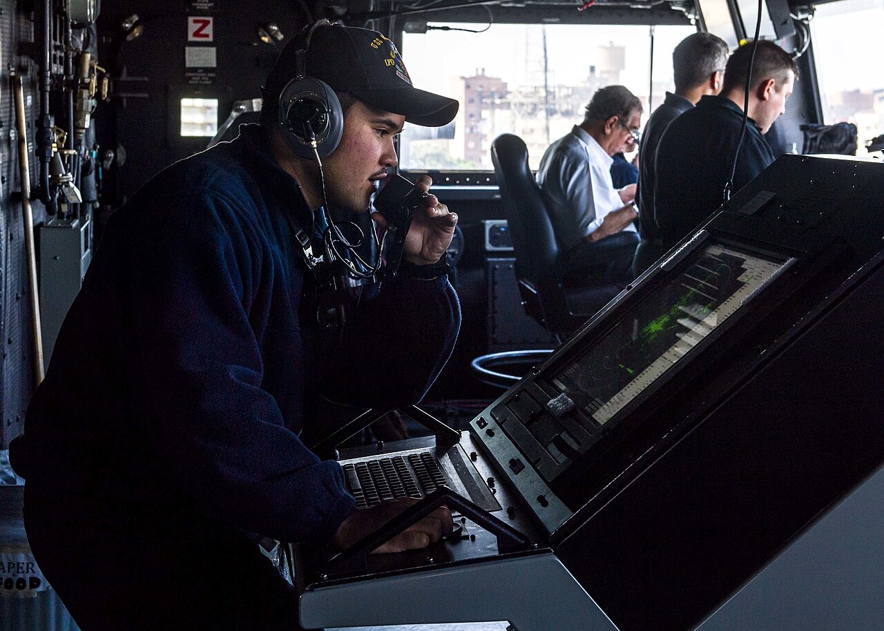 Marine radar operator using a communications handset beside an illuminated navigation display